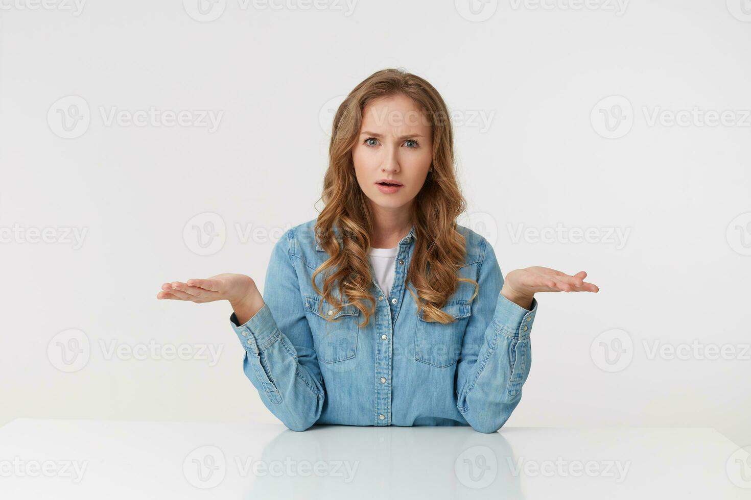 Confused young woman with long blond wavy hair, throwing up his arms in bewilderment, looks skeptically displeased indignantly with incomprehension, over white background. photo