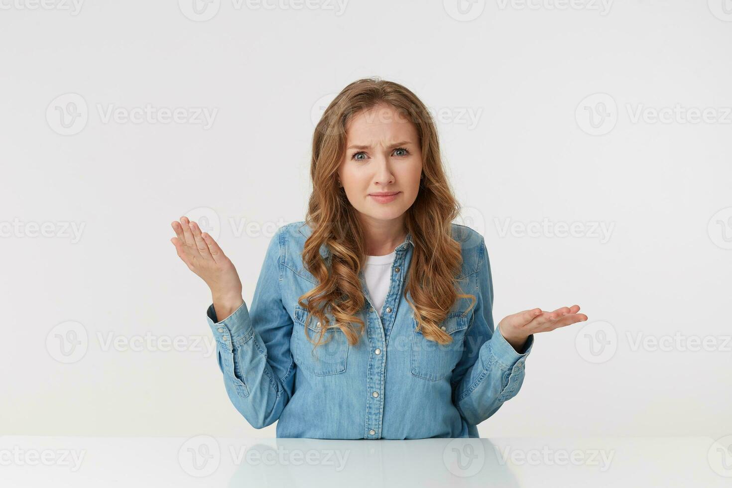 Serious young woman with long blond wavy hair, with folded hands, listens to her's boyfriend story with disbelief, with palms raised, expressing disappointment. photo