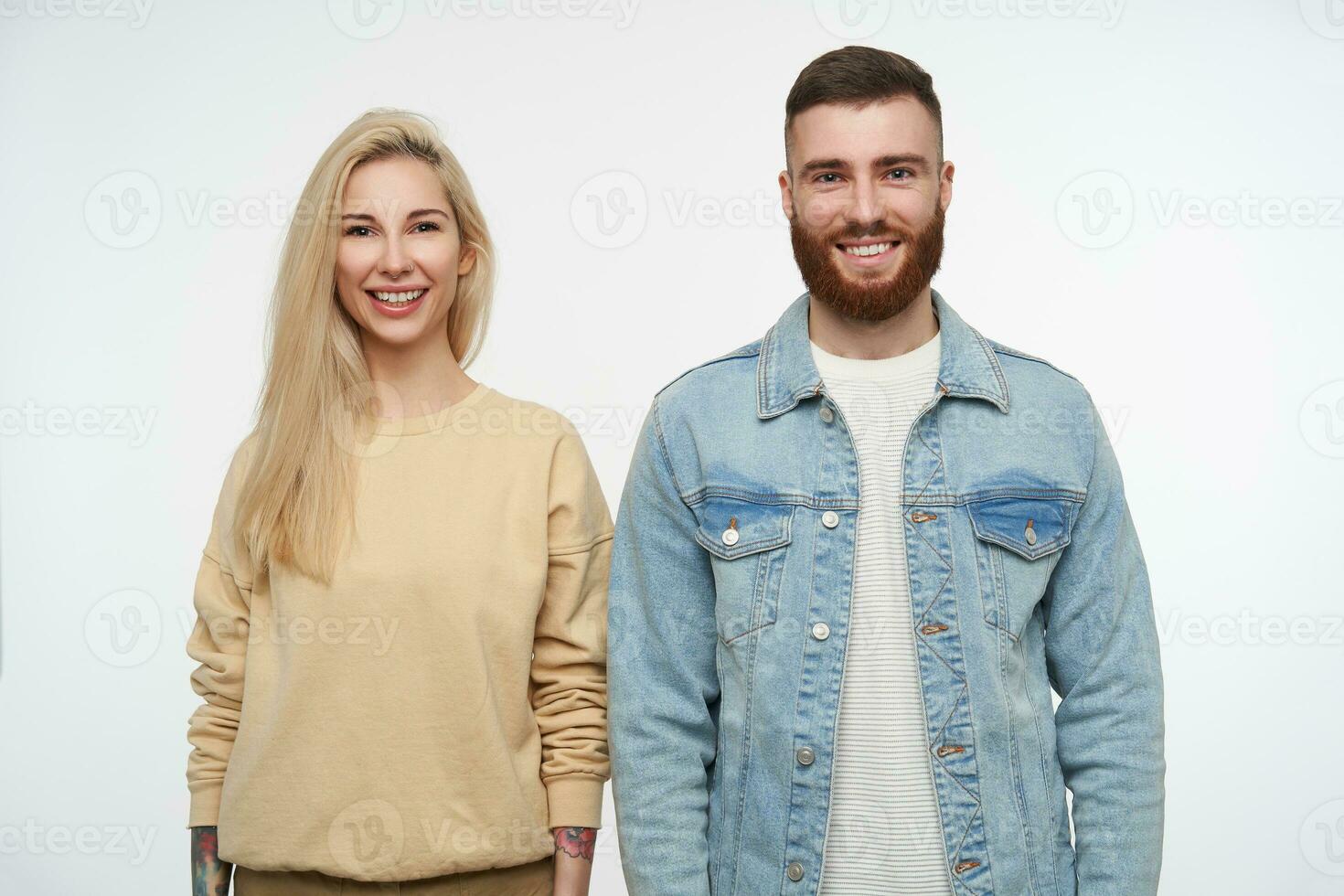 Cheerful young attractive couple dressed in casual clothes keeping their hands down while looking at camera with wide smile, isolated over white background photo
