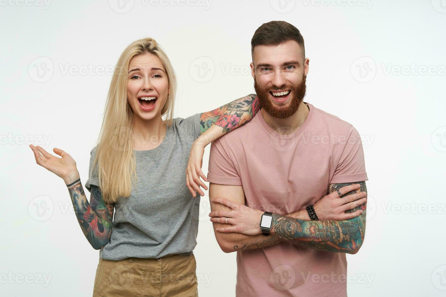 Joyful young lovely couple with tattooes laughing happily while rejoicing about something, wearing casual clothes while being isolated over white background photo