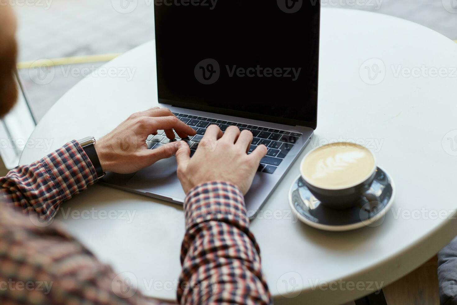 Men's hands are working on the keyboard of the laptop, nearly a gray cup of coffee on a white table. photo