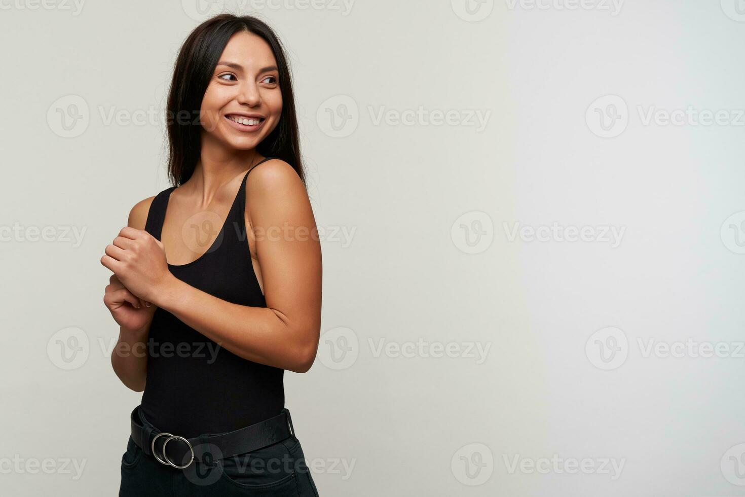 Happy attractive young brunette female with casual hairstyle looking cheerfully aside and folding raised hands together, smiling widely while posing over white background photo