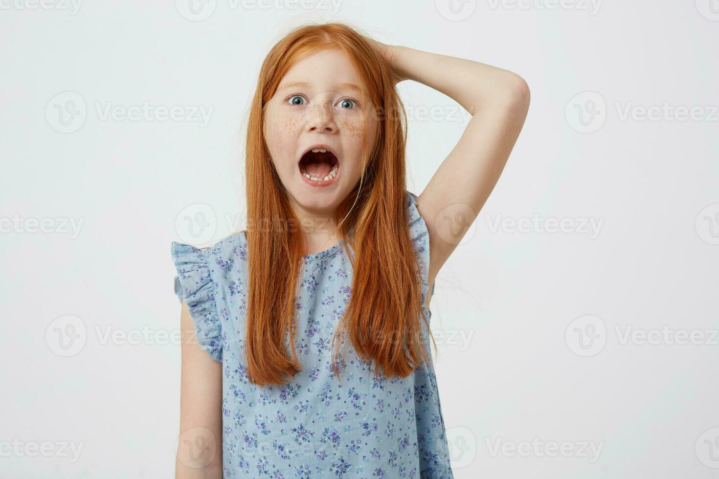 Portrait of screaming petite freckles red-haired girl, wears in blue dress, looks angry, stands over pink background. photo