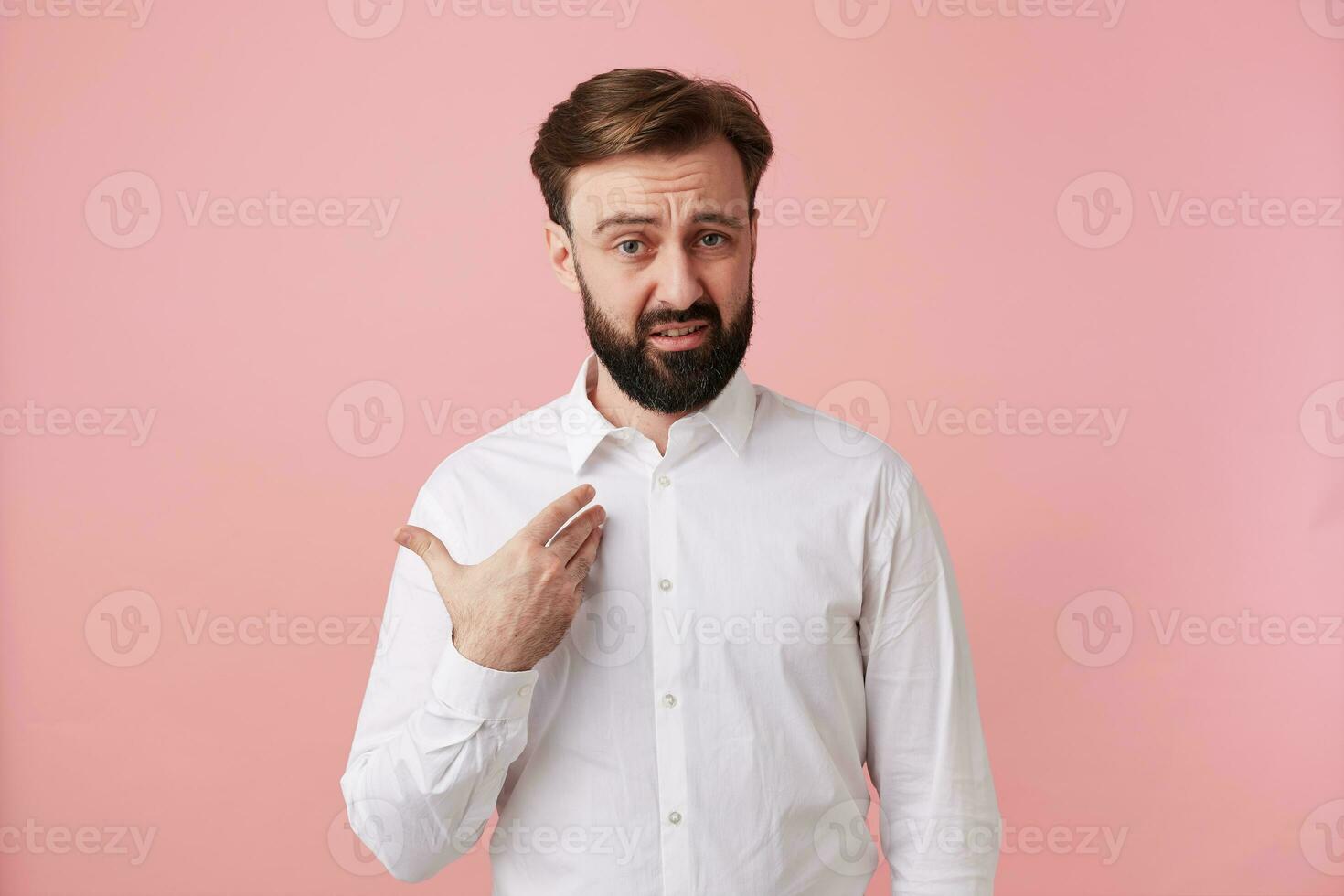 young bearded brunette man male guy with short haircut trendy hairstyle dressed in wearing white shirt formal clothes standing posing isolated over pink background photo