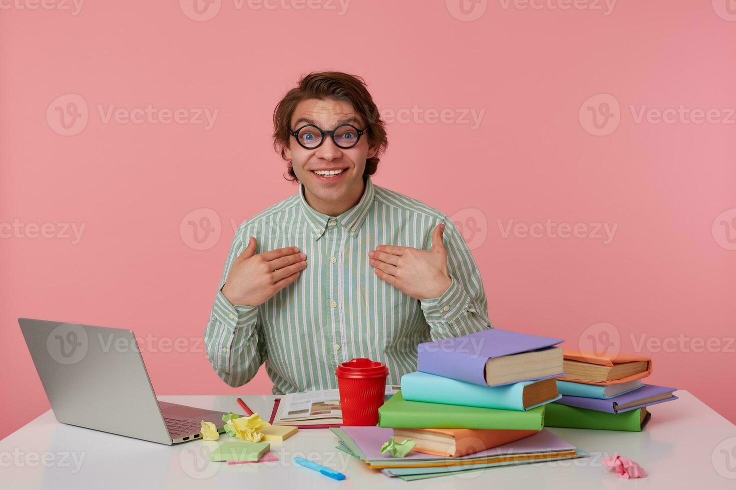Portrait of cheerful young man with dark hair looking at camera happily and raising eyebrows surprisedly, pointing to himself with raised palms, isolated posing over pink background photo