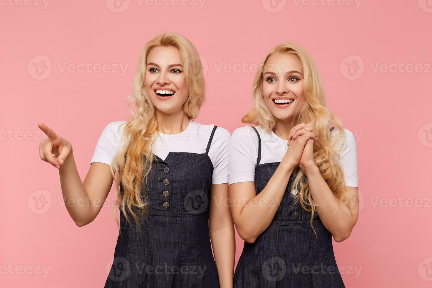 Happy young beautiful white-headed females with long loose hair showing their perfect white teeth while smiling cheerfully, standing over pink background photo