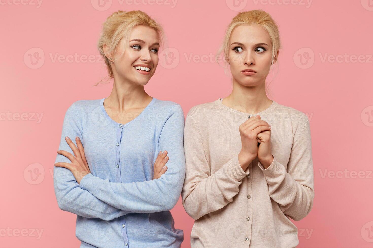 Young blonde lady mockingly looks at his sister isolated over pink background, who was frightened spider. photo