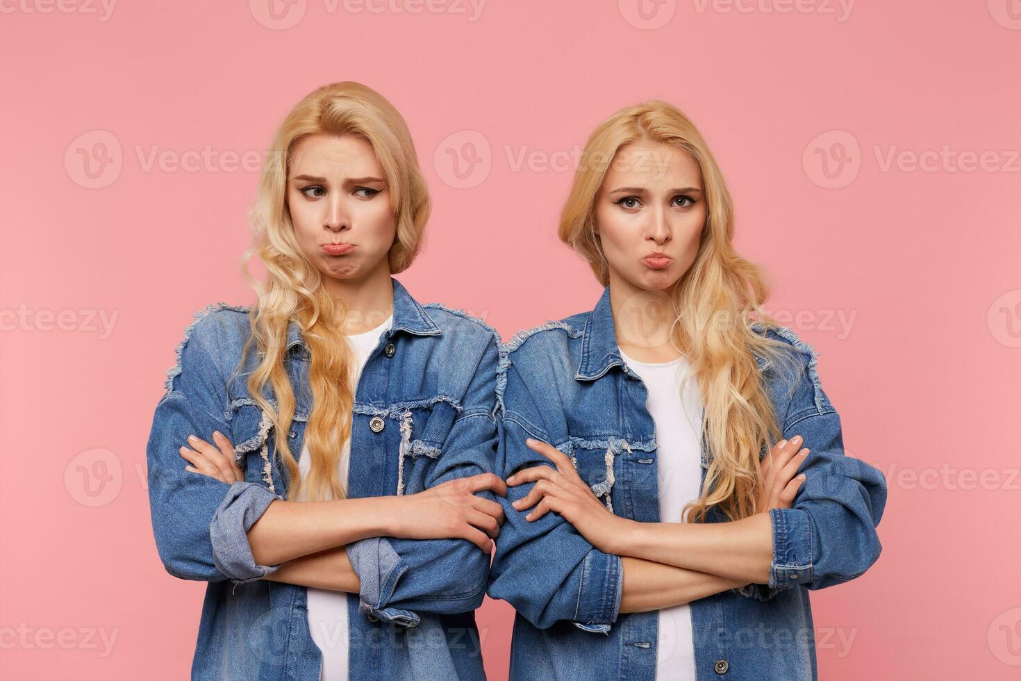 Offended young pretty blonde ladies with curls folding hands on chest while pouting sadly lips, dressed in casual clothes while posing over pink background photo