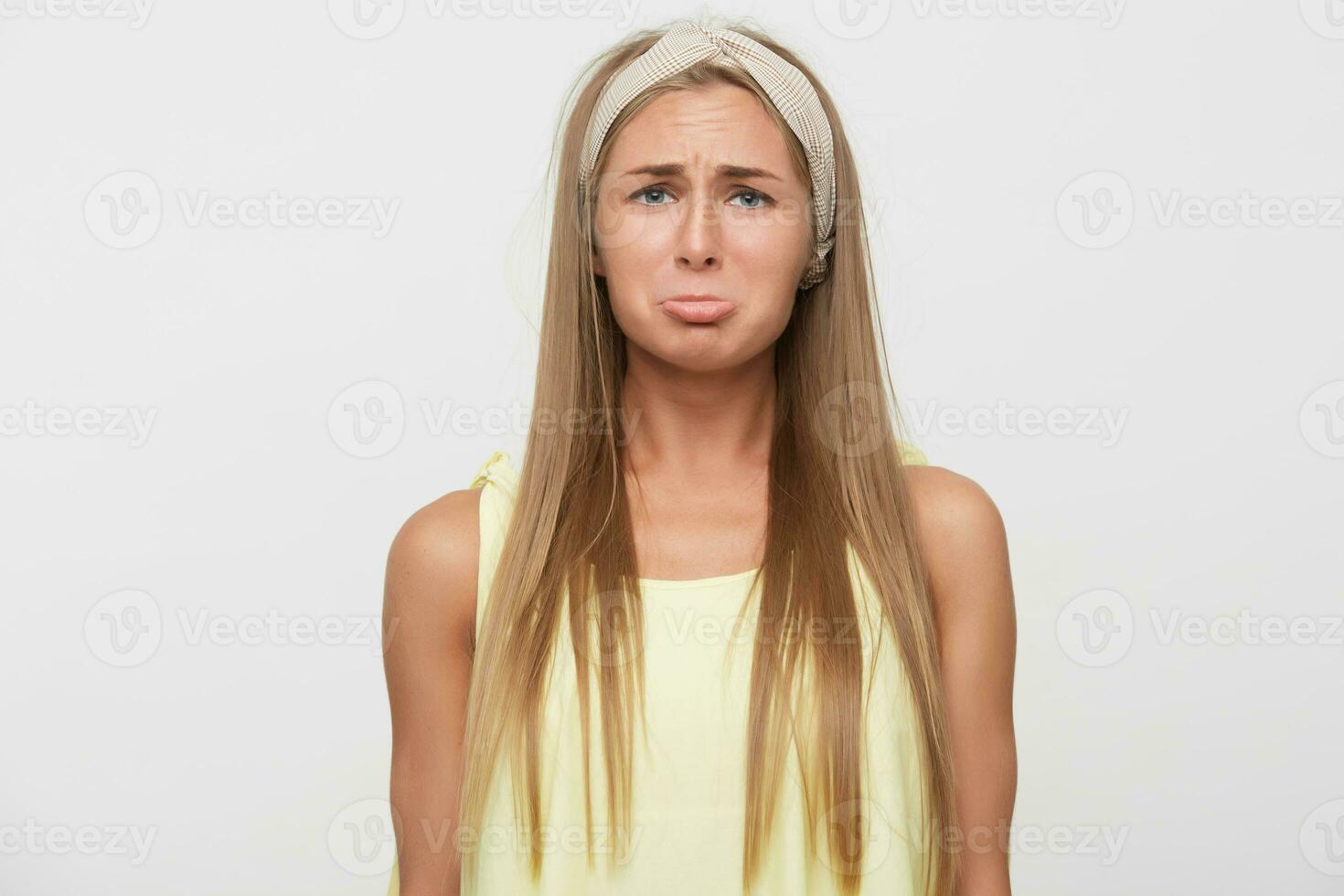 Offended young attractive long haired blonde lady with casual hairstyle pouting her lips while looking to camera with upset face, dressed in casual clothes while standing over white background photo