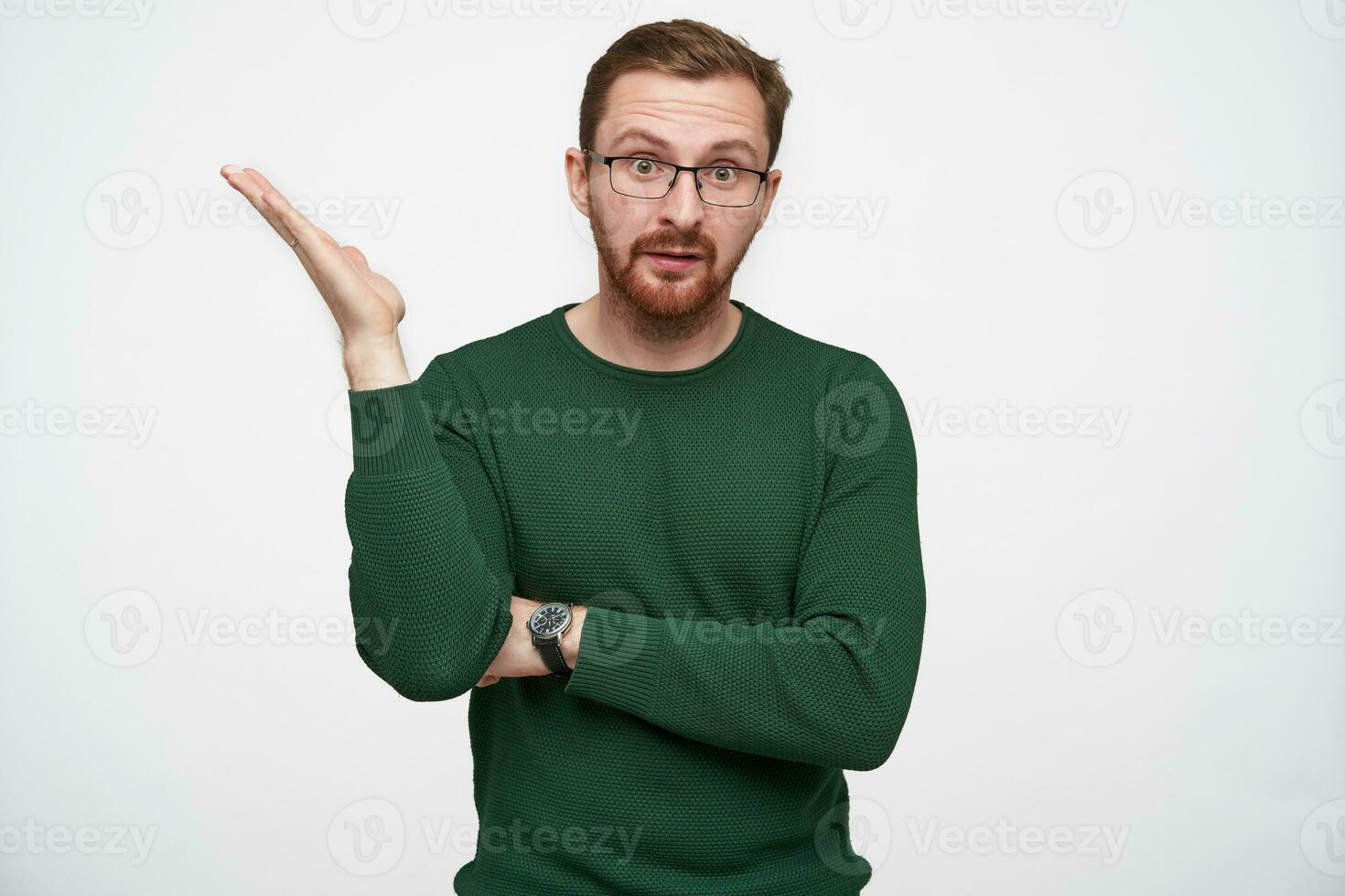 Confused young brunette man in glasses with short haircut raising emotionally hand and wrinkling forehead while looking at camera, isolated over white background photo