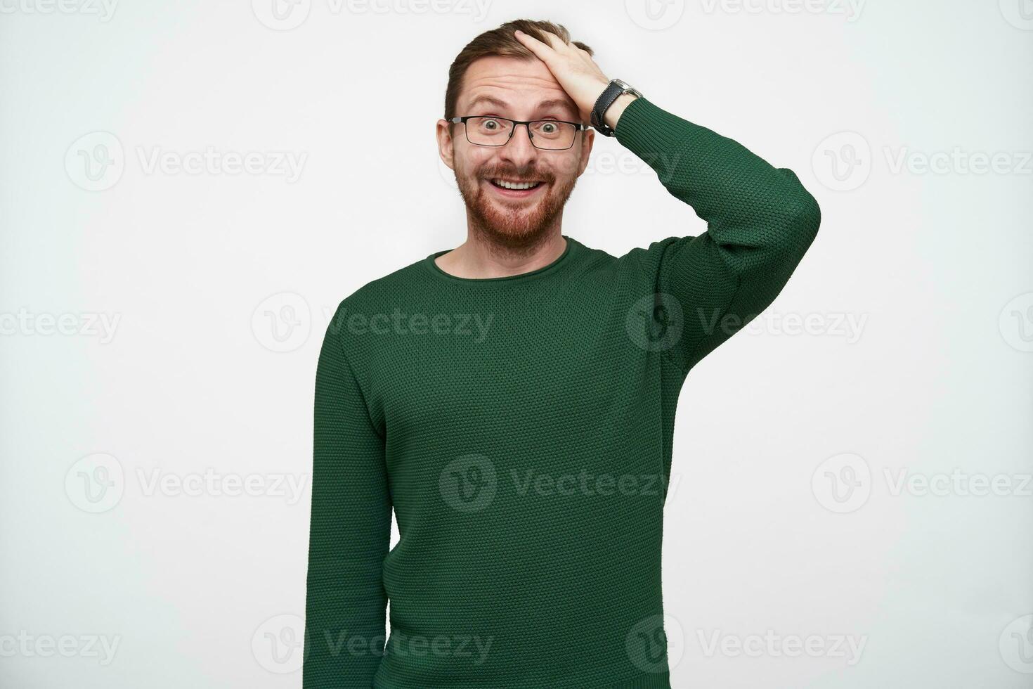 Amazed young handsome bearded man in eyewear rumpling his short brown hair and rounding surprisedly his eyes while looking at camera, isolated over white background photo