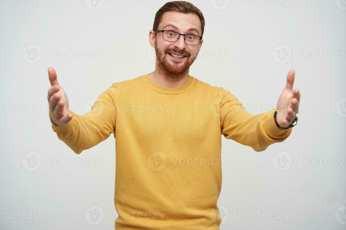 Cheerful young lovely brunette man in glasses with beard posing over white background with wide opened arms, looking positively at camera and smiling happily photo