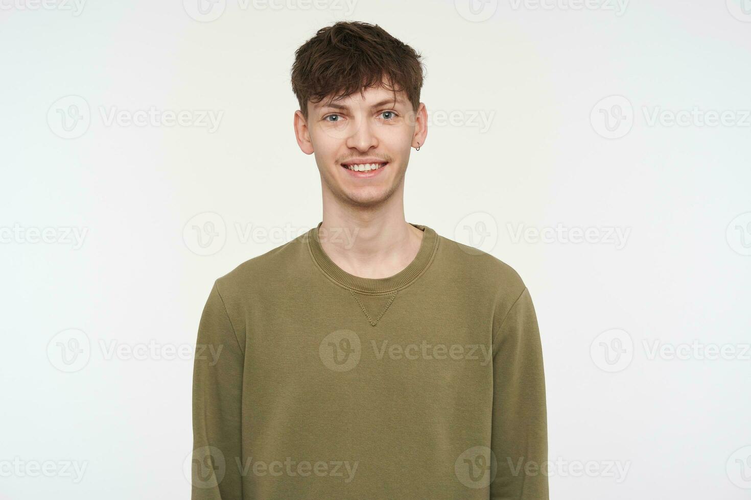 Young man, cool guy with brunette hair, piercing and bristle. Wearing khaki color sweater and have a confident smile. Emotional concept. Watching at the camera isolated over white background photo