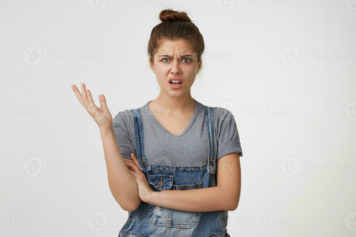 Close up of a young girl looks displeased, indignant, angry, one hand is raised up, one is crossed, her mouth is open, depicts outrage. Woman annoyed isolated on white background photo