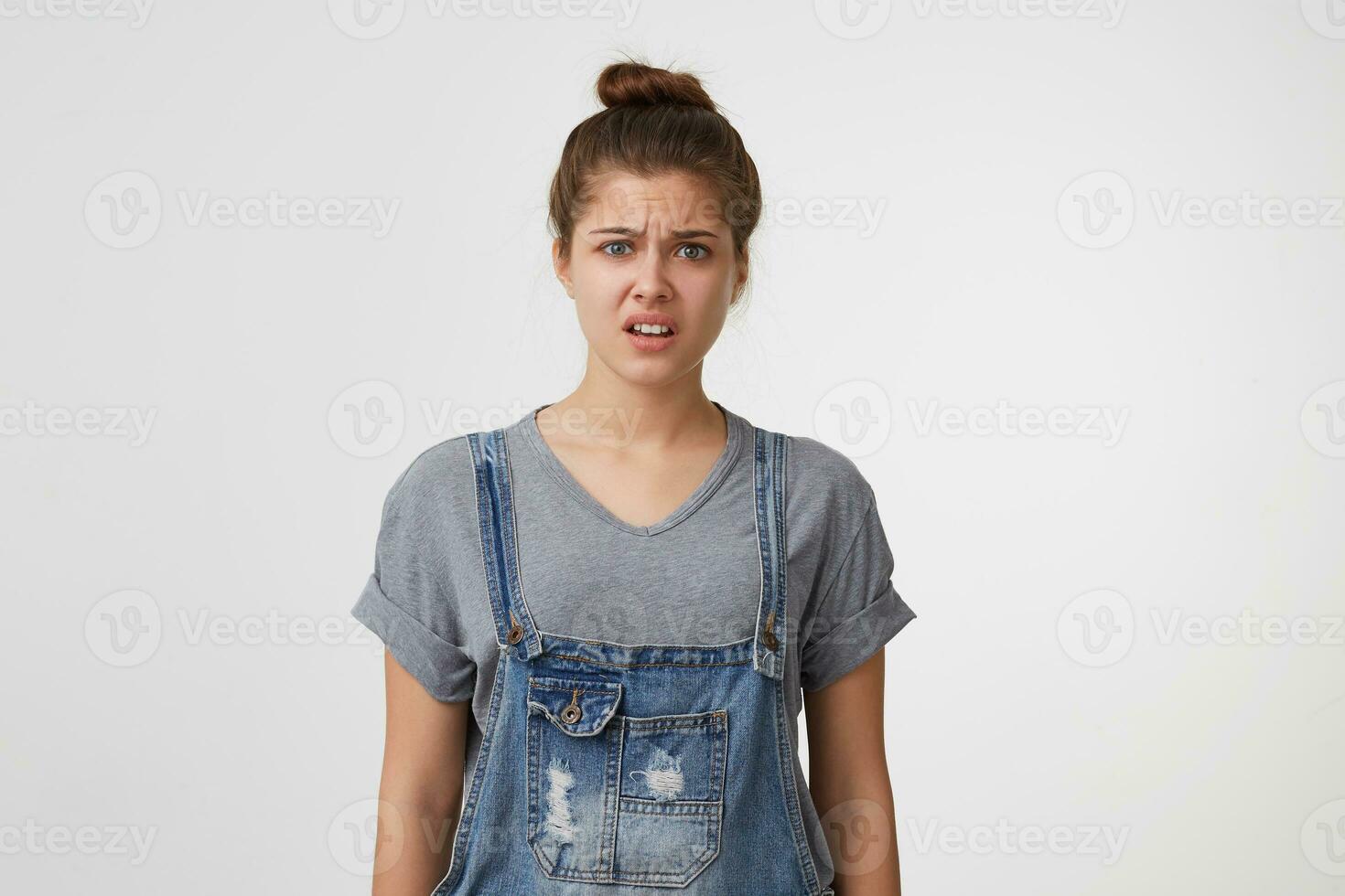 Young beautiful attractive girl dressed in a denim overall looks upset displeased unpleasantly surprised, angry, saw something disgusting. photo