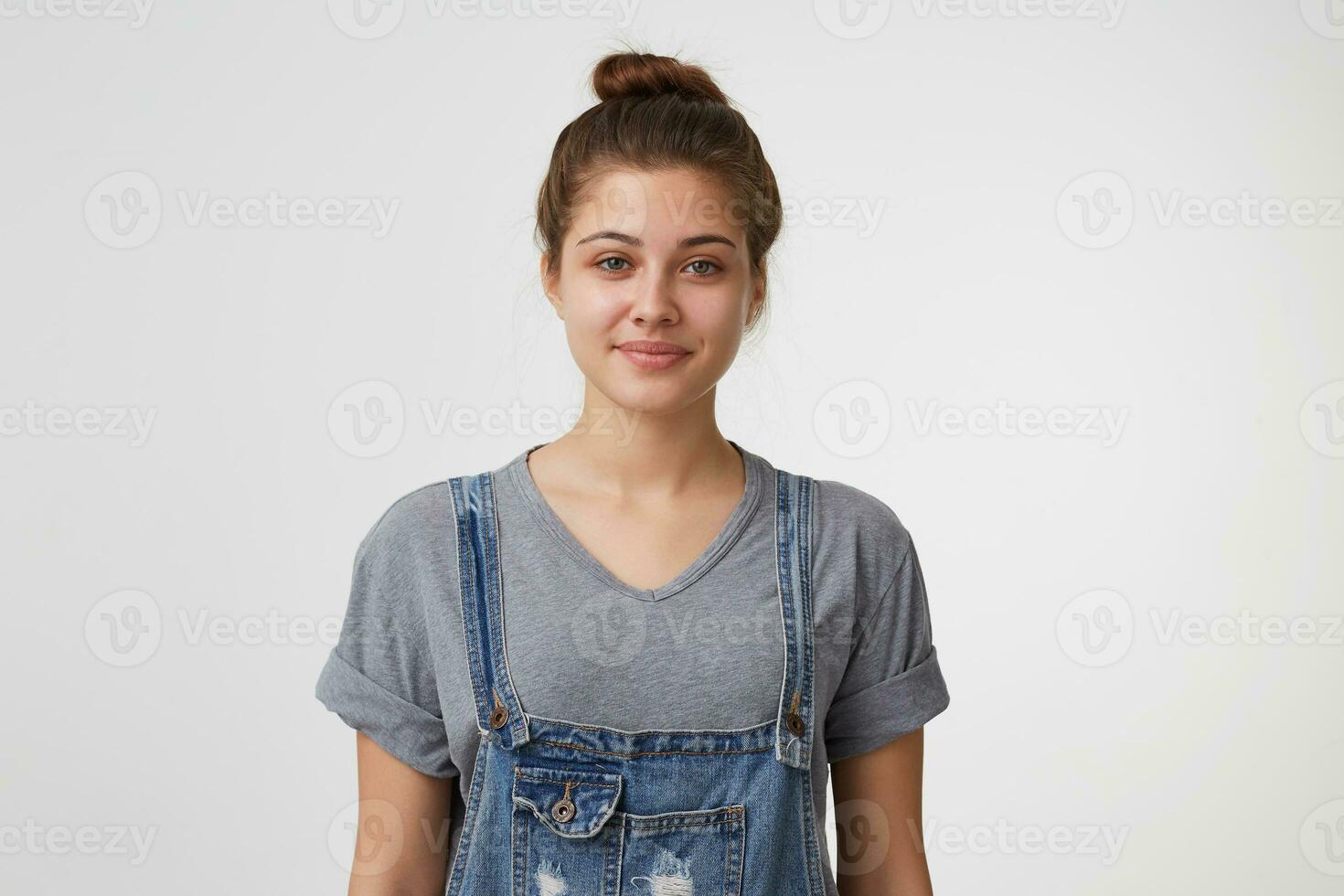 linda bonito y atractivo joven niña mira afable con un leve sonrisa vestido en mezclilla en general, pelo reunido en un bollo, aislado en un blanco antecedentes. foto