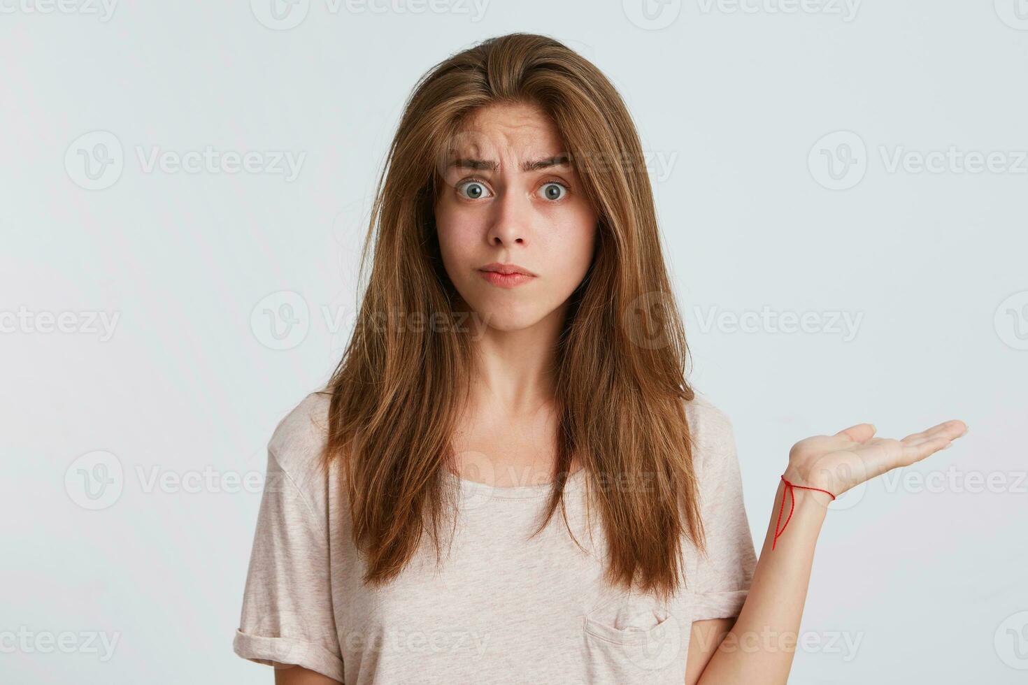 Closeup of amazed confused young woman with long hair wears t shirt standing and holding copy space on palm isolated over white background photo