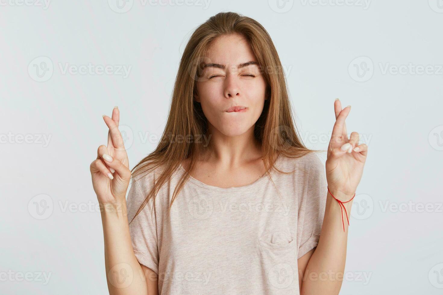 Closeup of pensive concentrated young woman with long hair wears t shirt keeps fingers crossed and making a wish isolated over white background photo