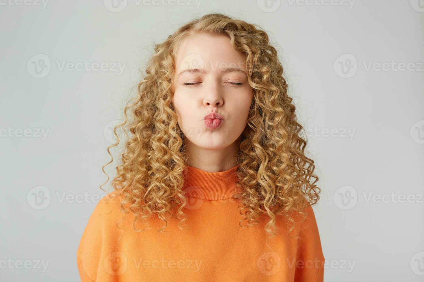 Portrait of pretty curly girl sending air kiss with pout lips and closed eyes isolated on white background, shows tender feelings.Sweet kiss directly to the camera. photo