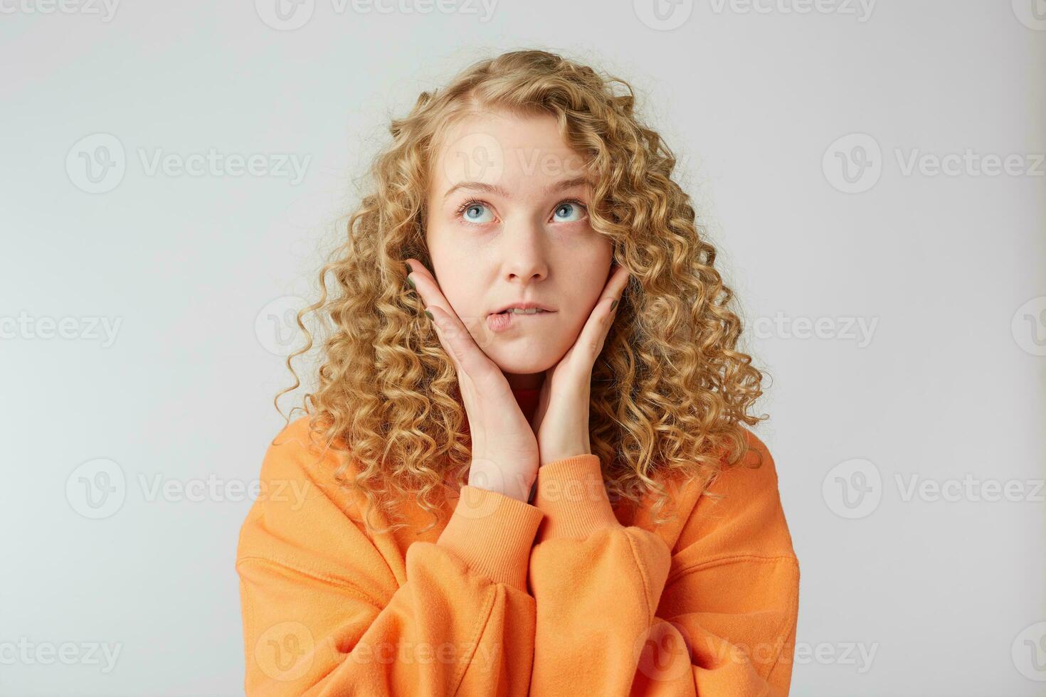 Sad thoughtful blonde thinking about her boyfriend, looks up, hovers in the clouds, makes plans, grieves about something, bit her lip, holds her palms near her face , isolated over white background photo