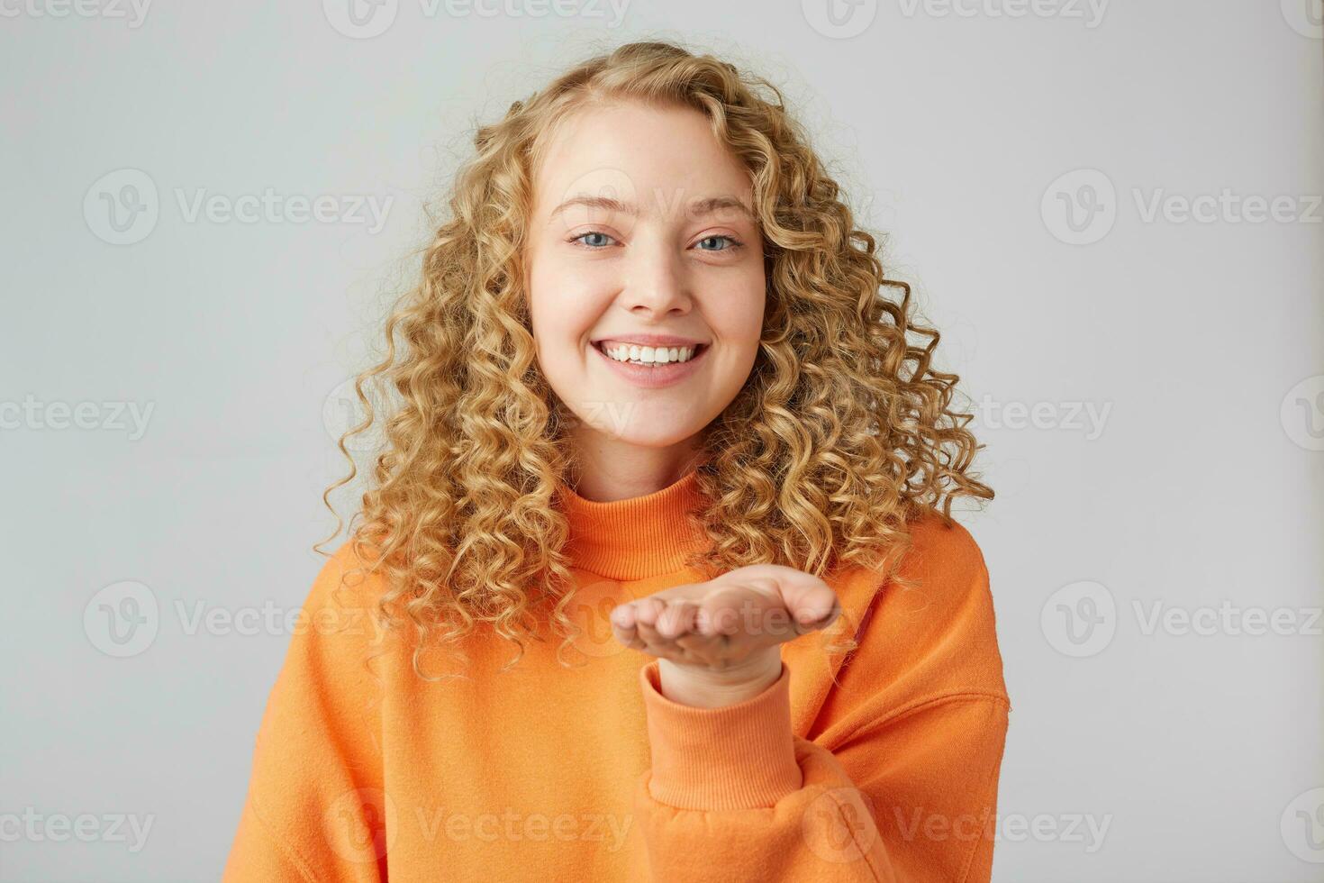 Romantic gestuers. Beautiful young curly blonde girl sending air kisses with charming smile. Studio shot on white background. photo