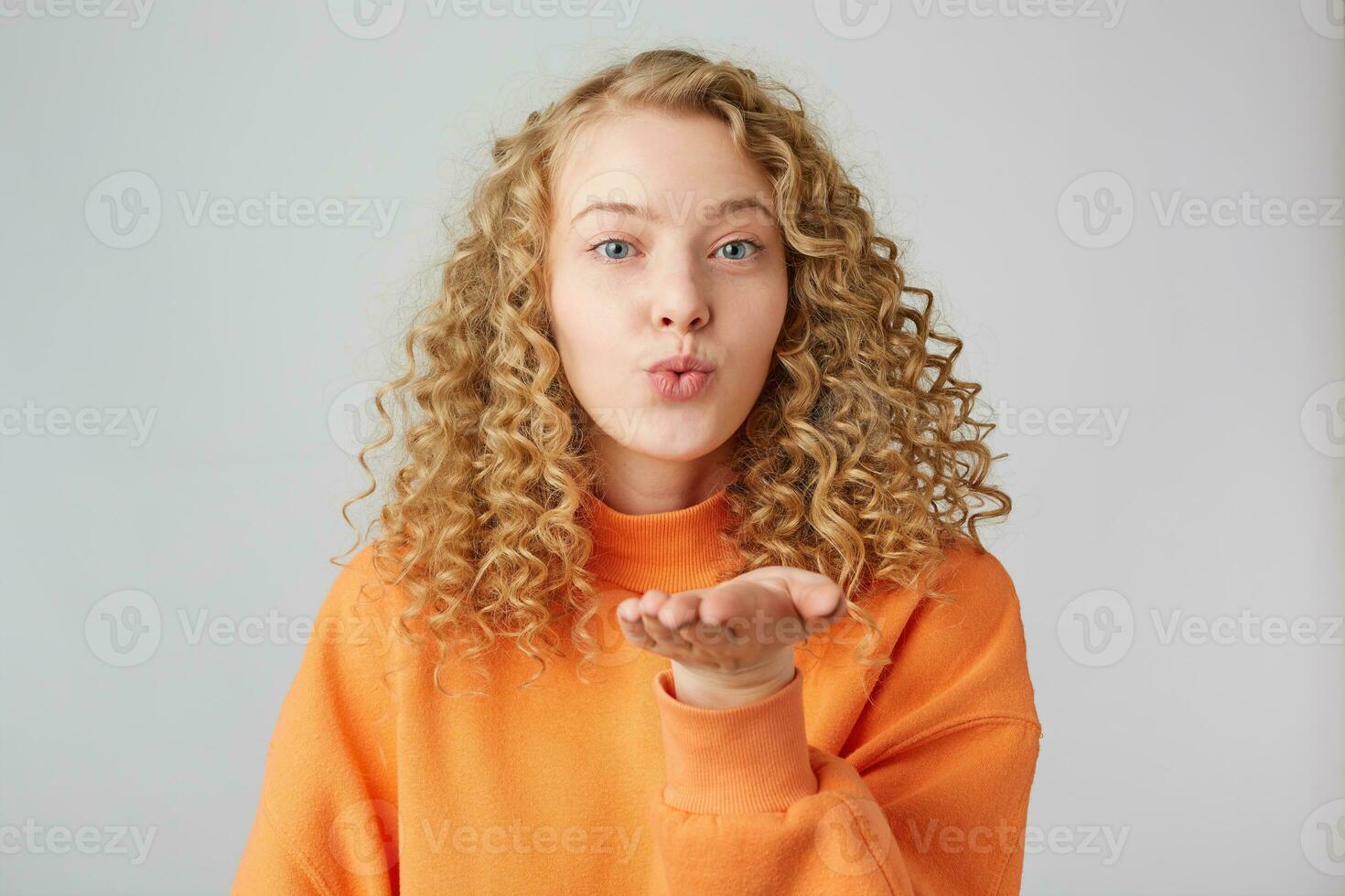 Blowing sending air kiss lovely pretty curly girl with pout lips isolated on white background, shows tender feelings.Sweet kiss directly to the camera. photo