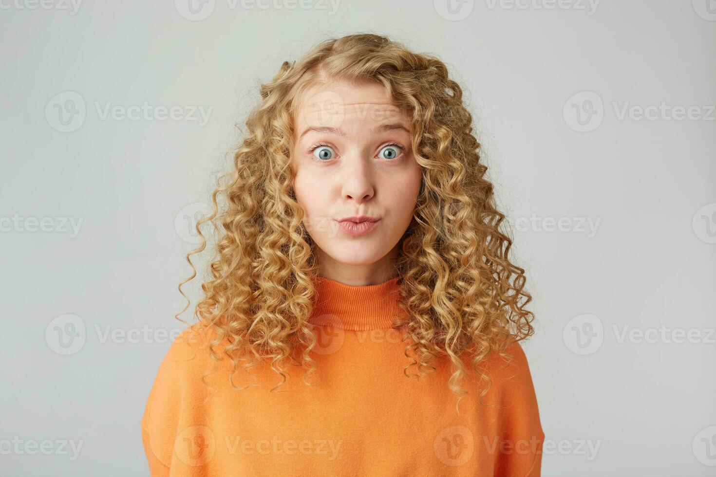 Headshot of pretty curly blonde girl staring in camera with popped eyes isolated on white background, looks with misunderstanding, carelessly, naive. photo