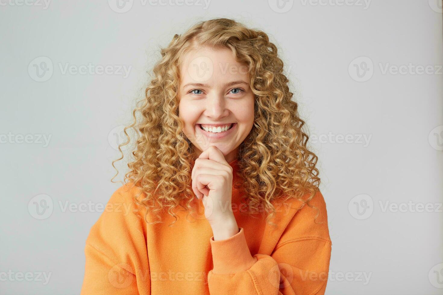 Cheerful emotional happy european female grins at camera, demonstrates white perfect teeth, keeps fist under chin, glad to recieve positive news, isolated over white wall photo