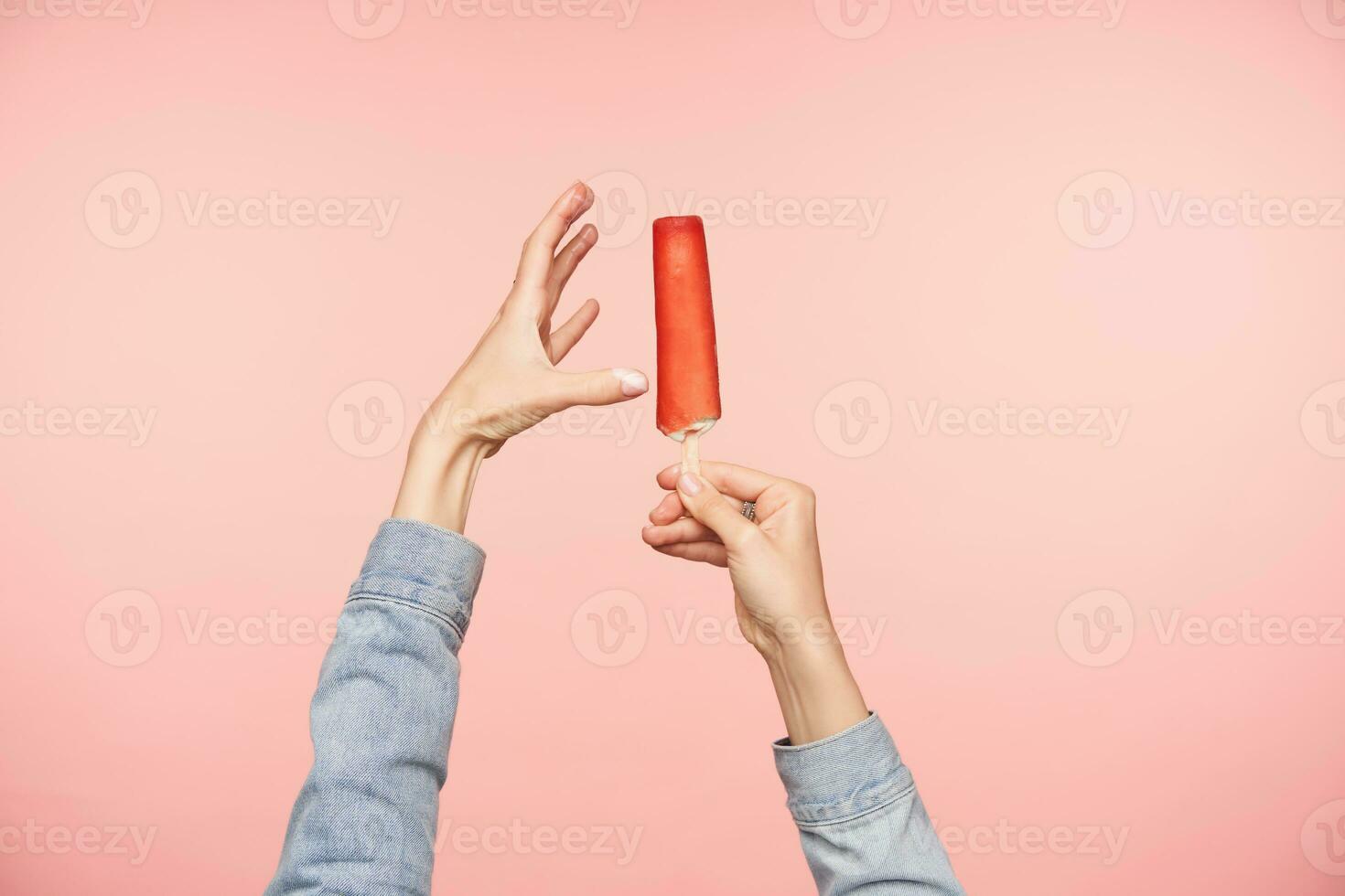 Studio photo of raised hands with red ice-cream demonstrating long length of it while posing over pink background. Human hands and food concept