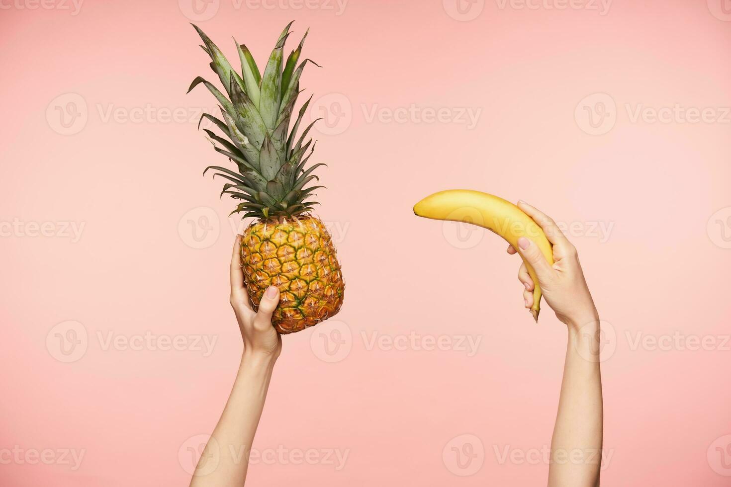 horizontal Disparo de bonito femenino manos siendo elevado mientras acuerdo en eso grande jugoso piña y banana, siendo aislado en contra rosado antecedentes foto