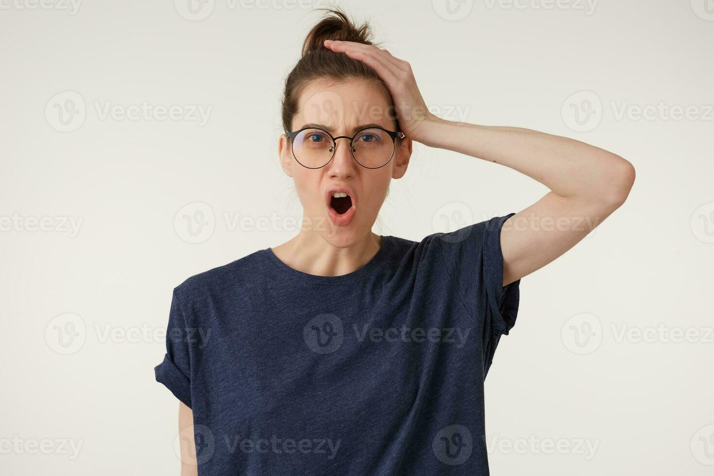 Angry, irate woman in glasses with mad grimace on her face,with mouth opened in shout, holding her head in horror from the mess that children have done, isolated over white background photo