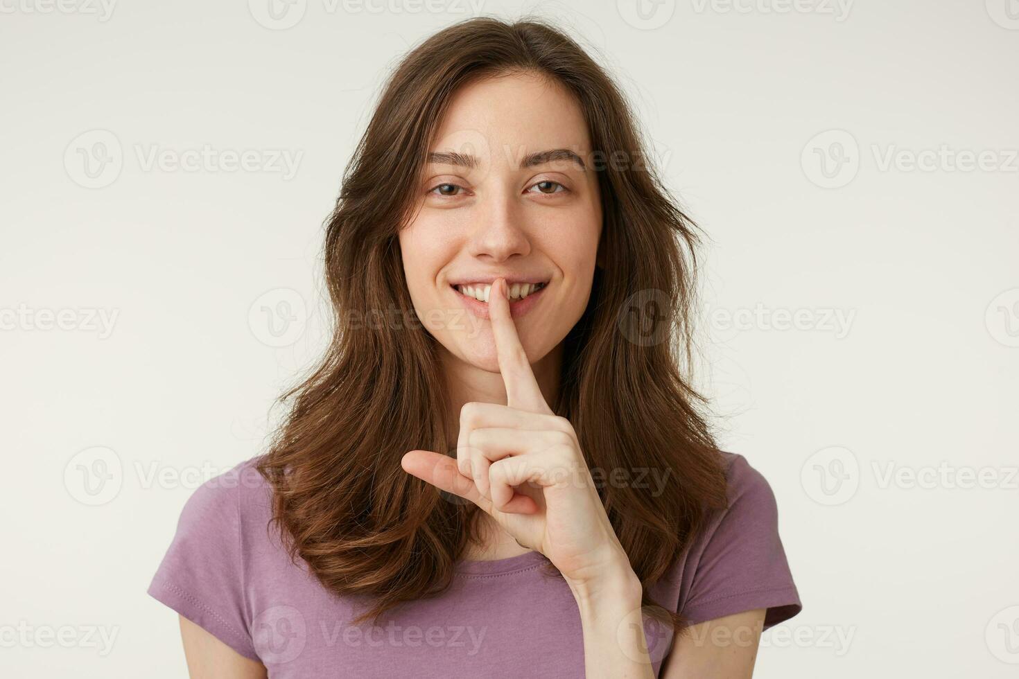 A cute mysterious girl with a playful smile flirting, demonstrates a gesture of silence. Holding an index finger near the mouth calls for privacy to be kept, secret. photo