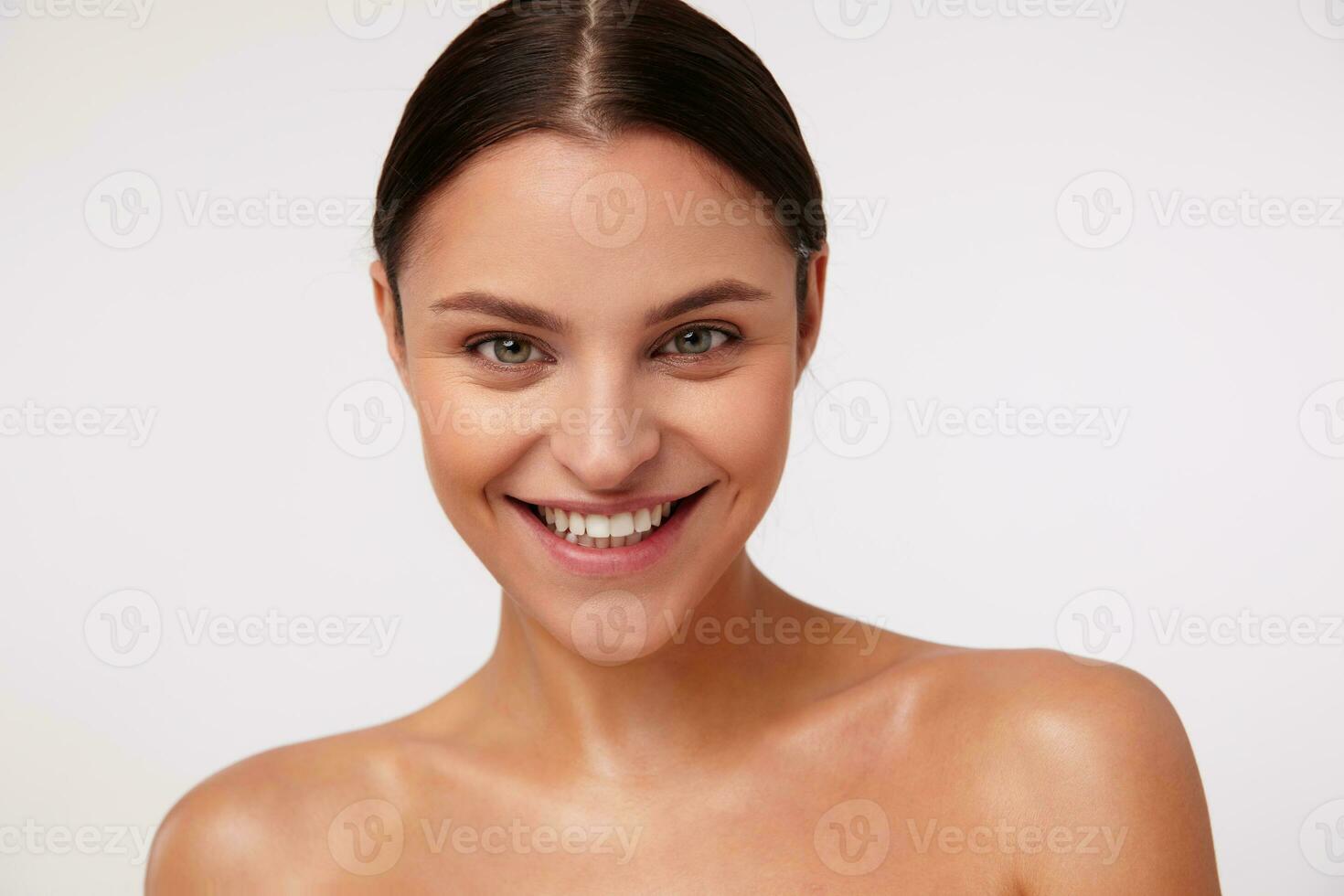 estudio Disparo de alegre encantador joven oscuro peludo hembra con natural maquillaje posando terminado blanco fondo, demostración su agradable emociones y sonriente extensamente a cámara foto