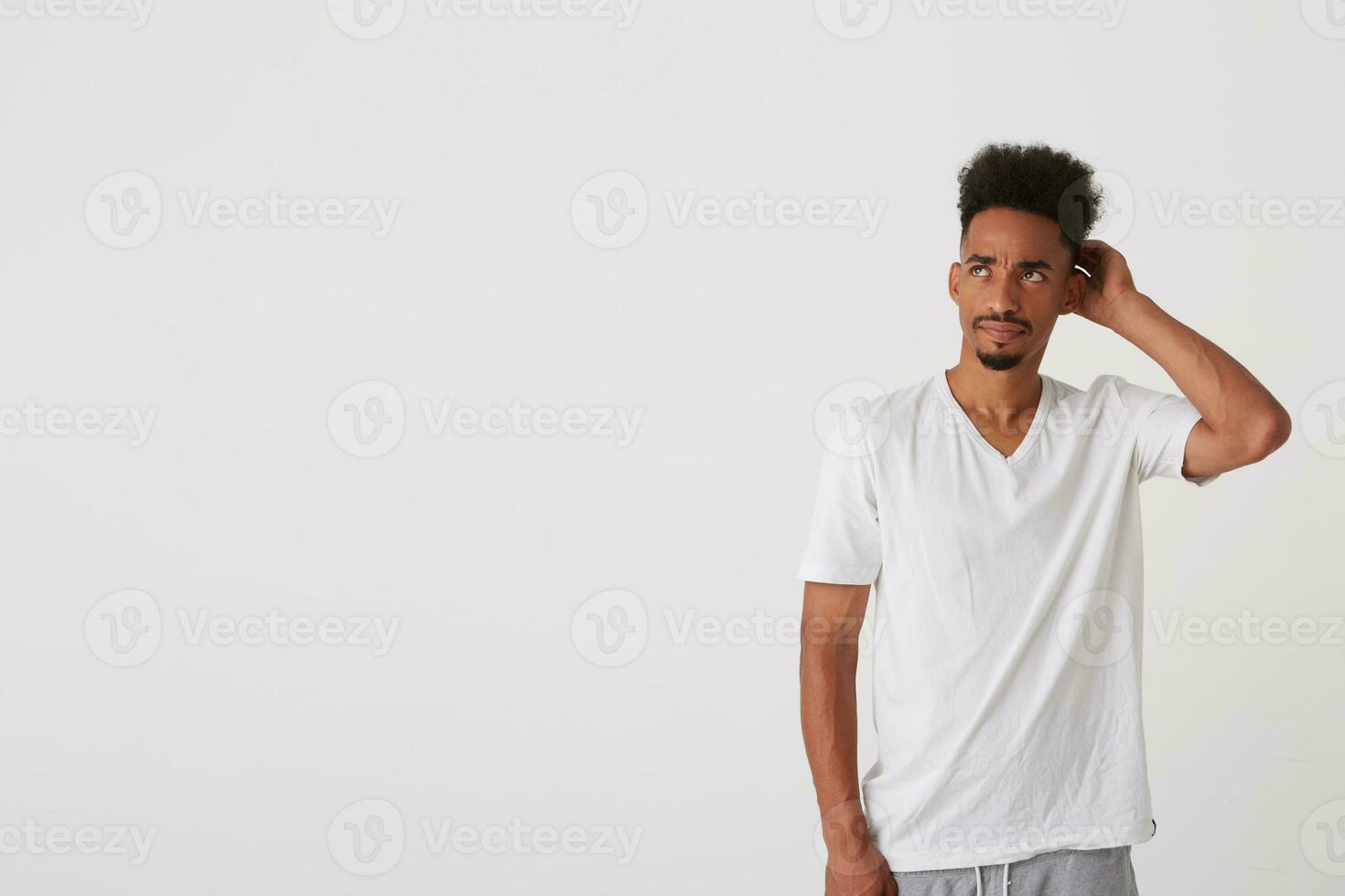 Bewildered young attractive short haired brunette man with dark skin raising head to his head while looking confusedly aside, isolated over white background photo