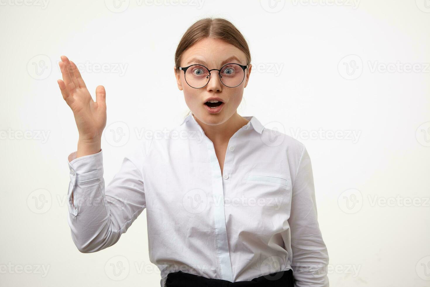 Agitated young blonde woman in glasses rounding amazedly her eyes and keeping palms raised while looking surprisedly at camera, isolated over white background photo