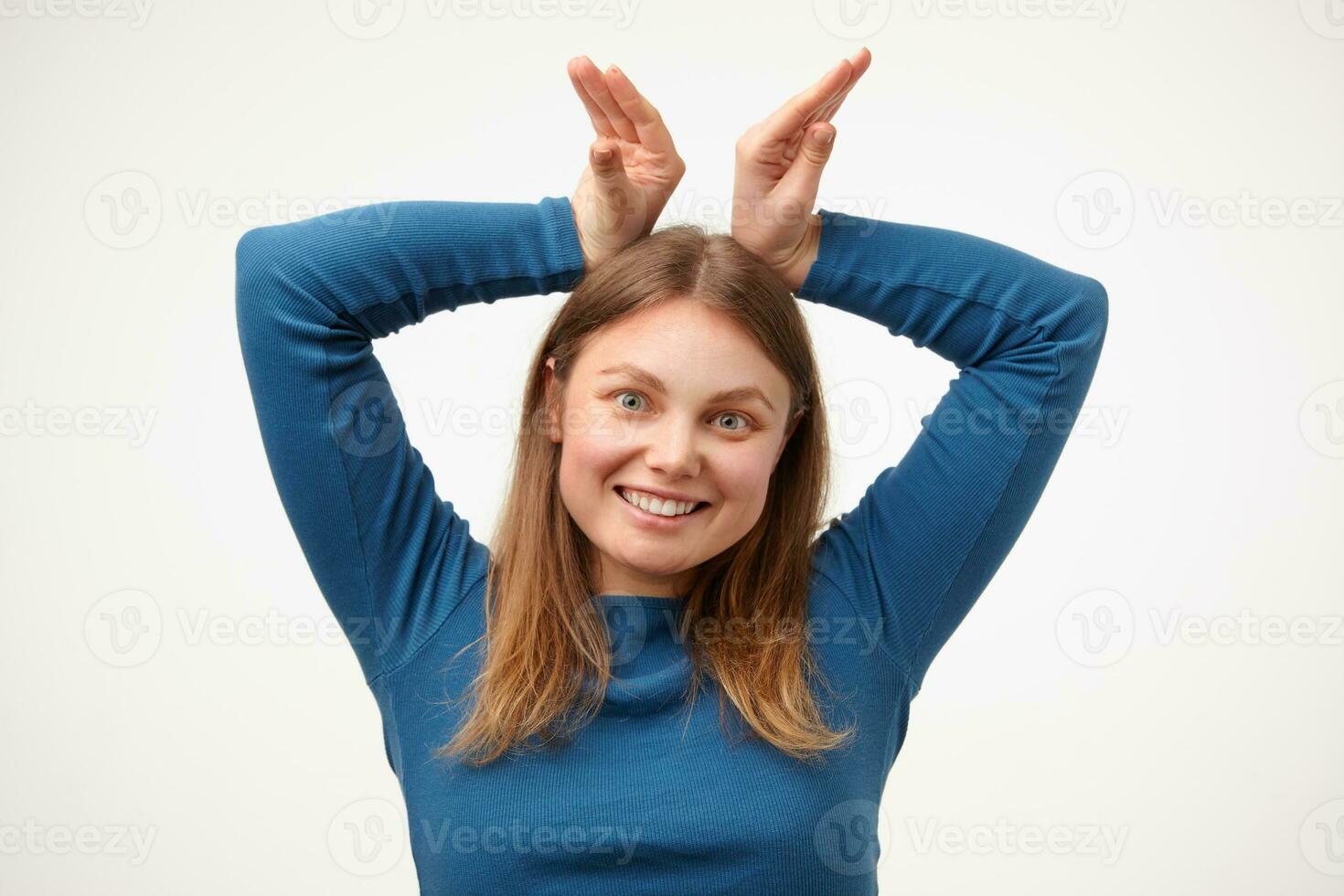 Joyful young pretty white-headed woman with casual hairstyle keeping raised hands above her head and smiling happily at camera while having fun, isolated over white background photo