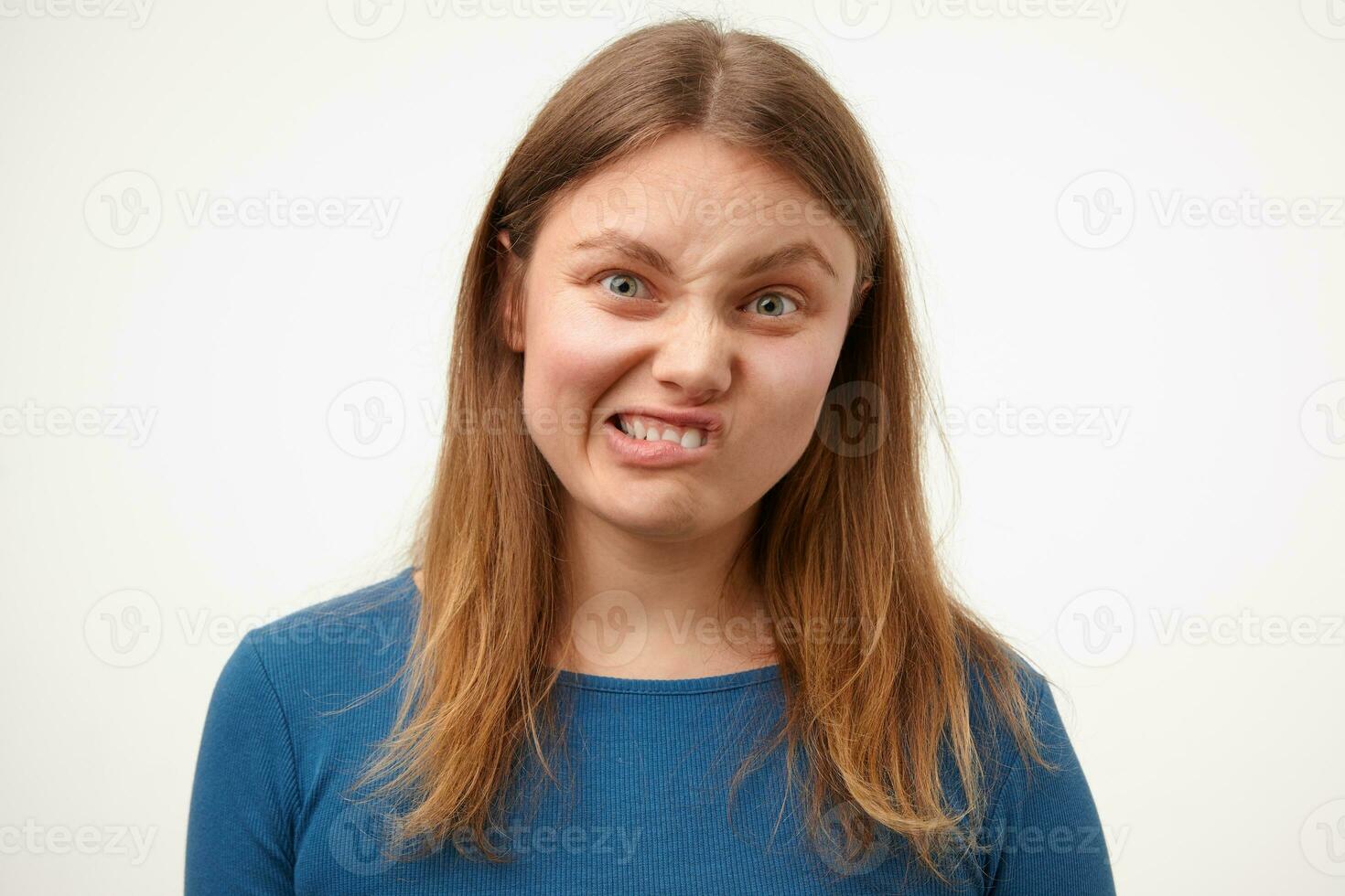 Indoor shot of young confused white-headed woman with natural makeup grimacing her face while looking at camera, standing against white background photo