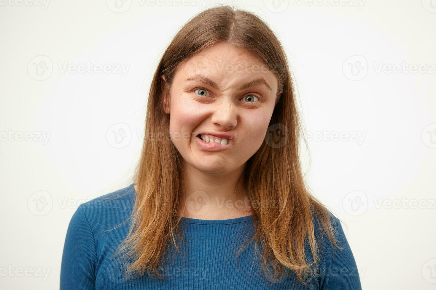 Indoor shot of young confused white-headed woman with natural makeup grimacing her face while looking at camera, standing against white background photo