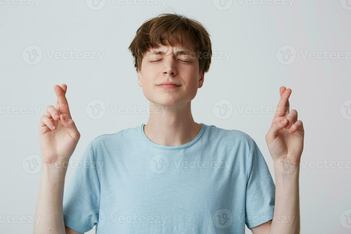 positivo fiel joven chico, clausura ojos con esperanza, cruce dedos mientras haciendo desear, falto alguna cosa y preguntando Dios a cumplir sueño, vestido casual aislado terminado blanco antecedentes foto