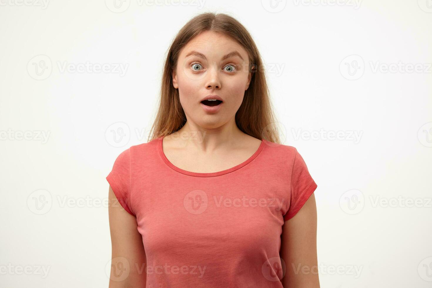 Bemused young white-headed woman with loose long hair keeping mouth opened while looking amazedly at camera, posing over white background with hands down photo