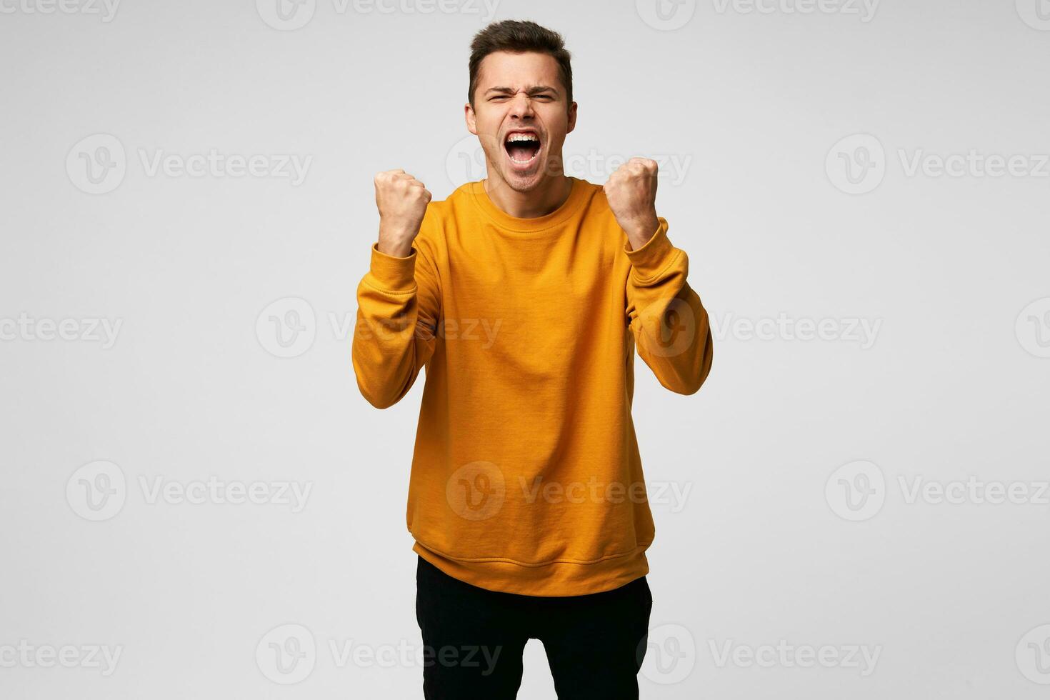Young happy man with really impressive achievements, giving a fists up gesture of victory, rewarded, won a good prize, successful deal, positive news, screaming with happiness, over white background photo