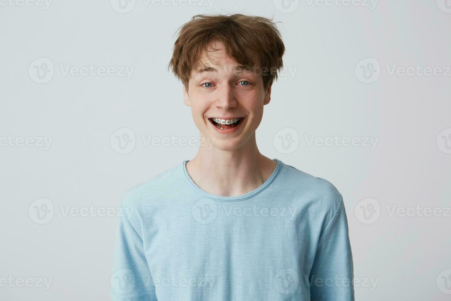 Incredibly, over-measure joyful guy smiles broadly, shows enthusiasm and passion, disheveled hair, mouth wide opened with braces on teeth, feels glad, over white background photo