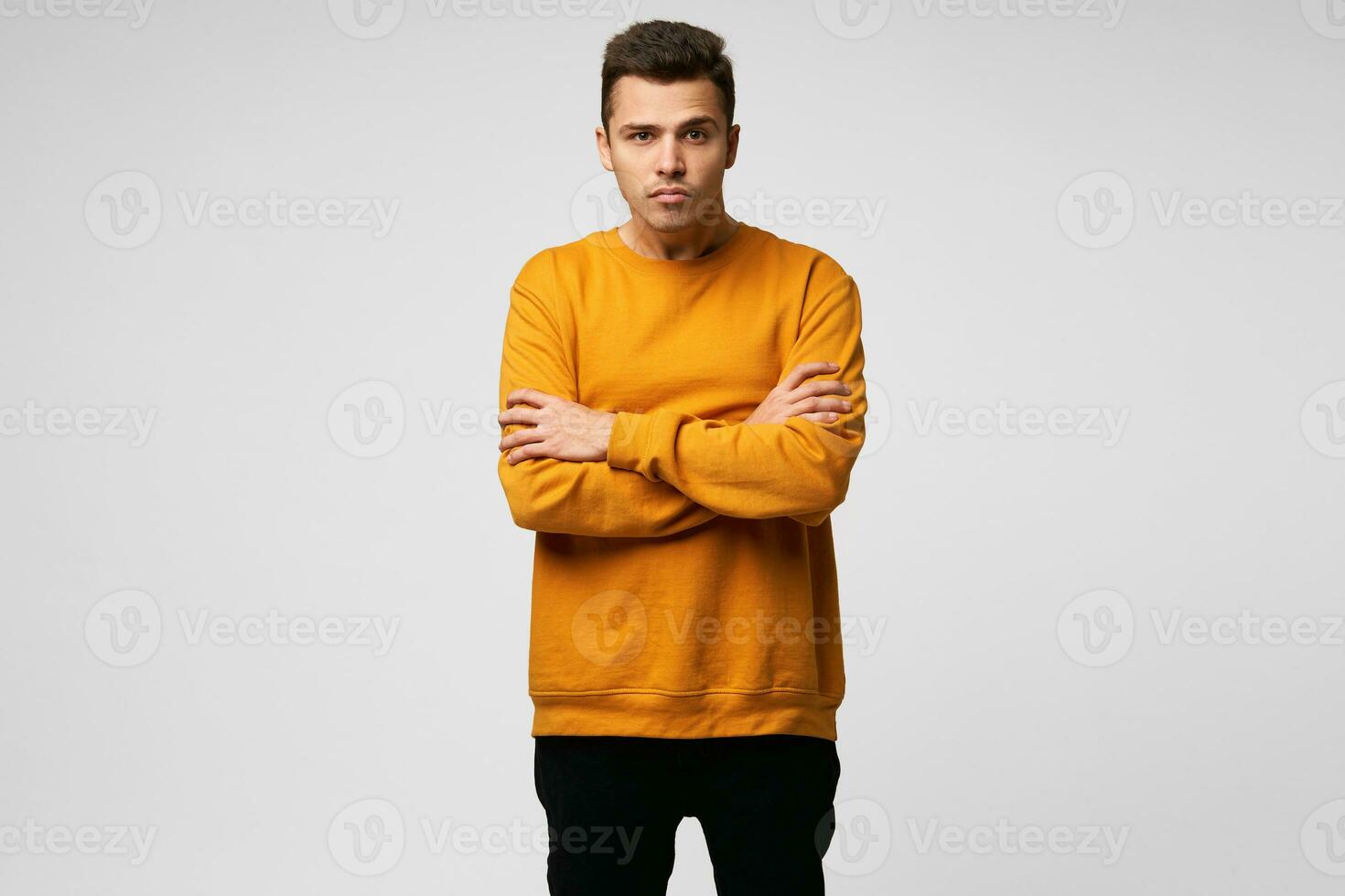 Man stands stooping, his head is pressed into his shoulders, his neck is stretched forward, his arms are crossed, looking straight, looking at something in front, face without emotion,white background photo