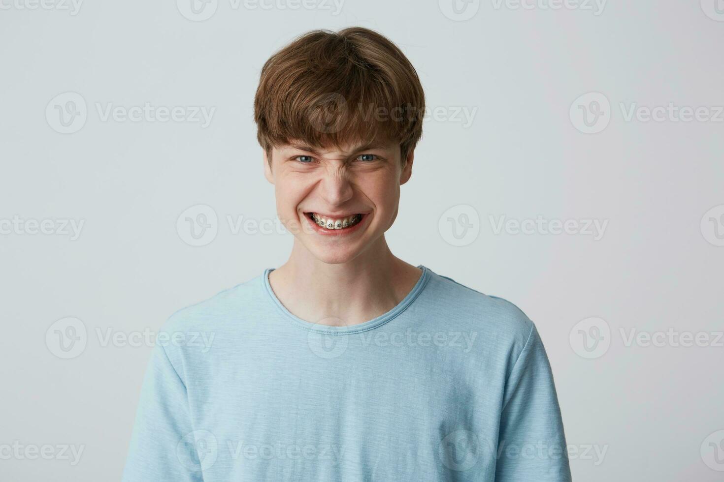 Angry, upset, irate teenager bares his teeth showing braces, an grumpy grimassa on his face, ready to argue and swear, wants to gain respect, show strength, isolated over white background photo