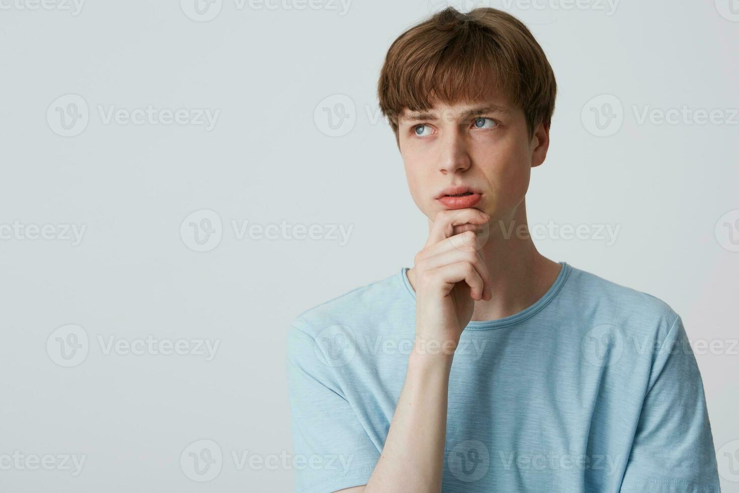 enfocado joven hombre en azul camiseta, mantiene brazo en barbilla y mira pensativamente lejos, siendo confuso y cuestionado, pensando qué hacer a resolver el problema, preocupado, terminado blanco antecedentes foto