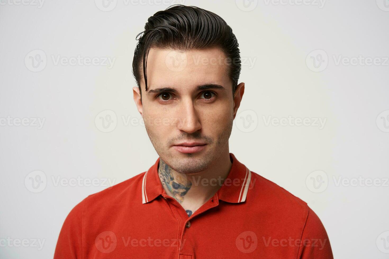 Headshot of a confident guy without emotions. Emotionless man stays calm, with great self-control, in a red polo looking to the camera, isolated over white background photo