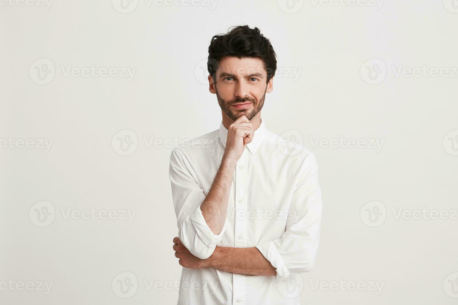 Portrait of thoughtful attractive young businessman with bristle wears shirt looks pensive and confident isolated over white background Keeps hands folded photo