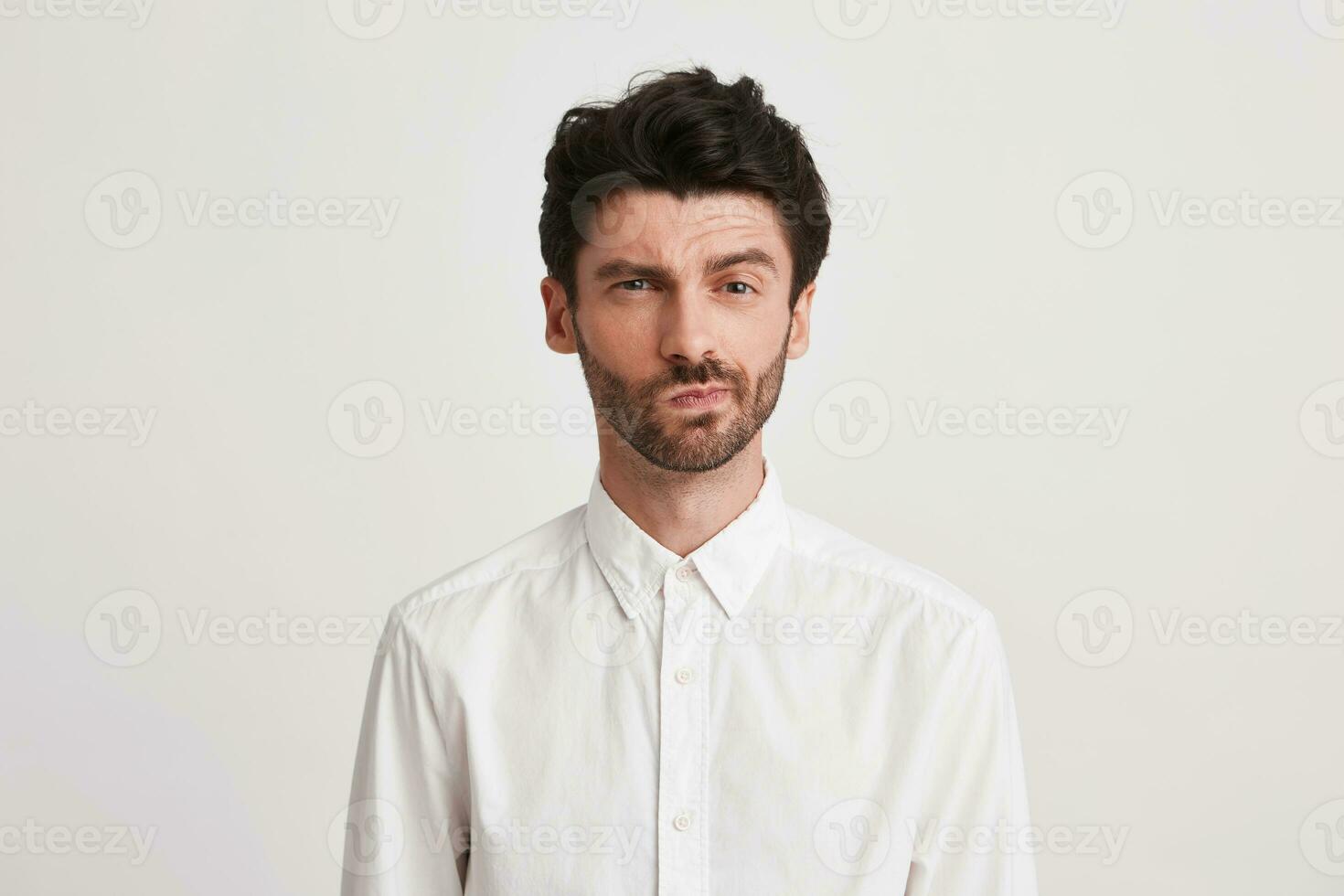 Closeup of serious displeased young businessman with bristle wears shirt looks pensive and dissatisfied isolated over white background photo