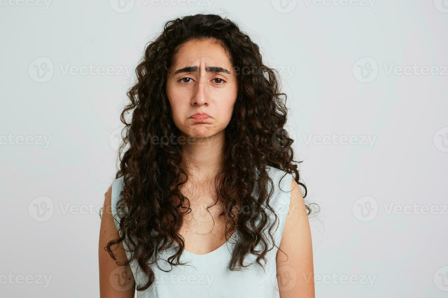 retrato de trastornado Deprimido joven mujer con largo oscuro Rizado pelo mira triste y decepcionado aislado terminado blanco pared siente desesperado y cansado después difícil trabajando día foto