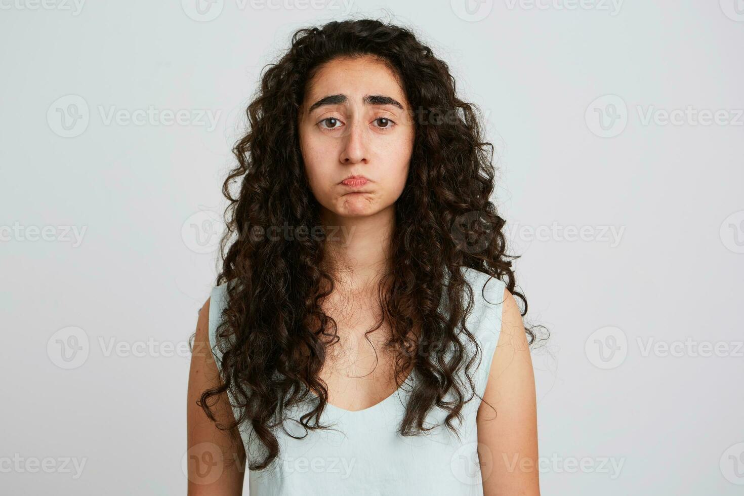 Closeup of sad unhappy young woman with long dark curly hair feels disappointed and have problems isolated over white wall Looks upset and depressed photo